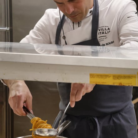 Um chefe a empratar massa num balcão de serviço, numa cozinha de hotel.