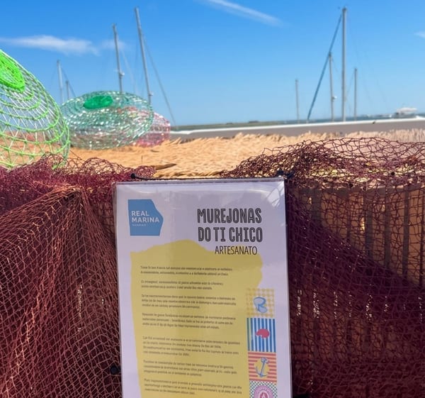 O cartaz da exposição “Murejonas do Ti Chico” preso a uma rede de pesca, junto à água.