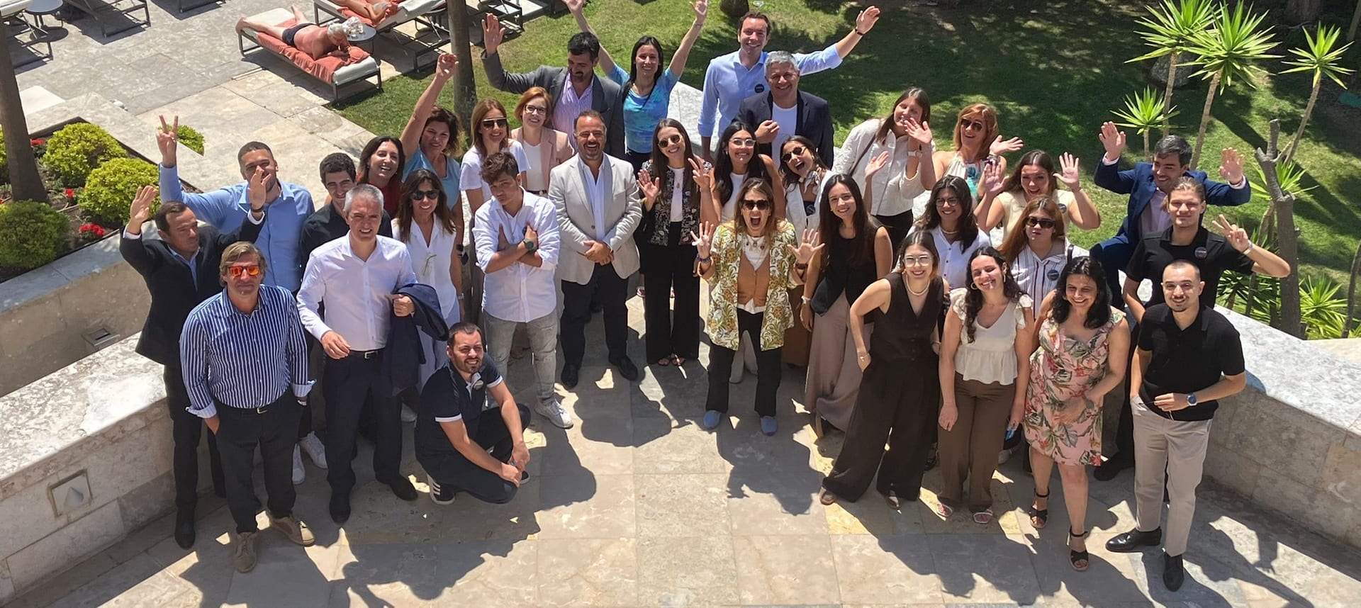 As equipas do Grupo reunidas num terraço de hotel sobre a piscina, a acenar para a câmara.