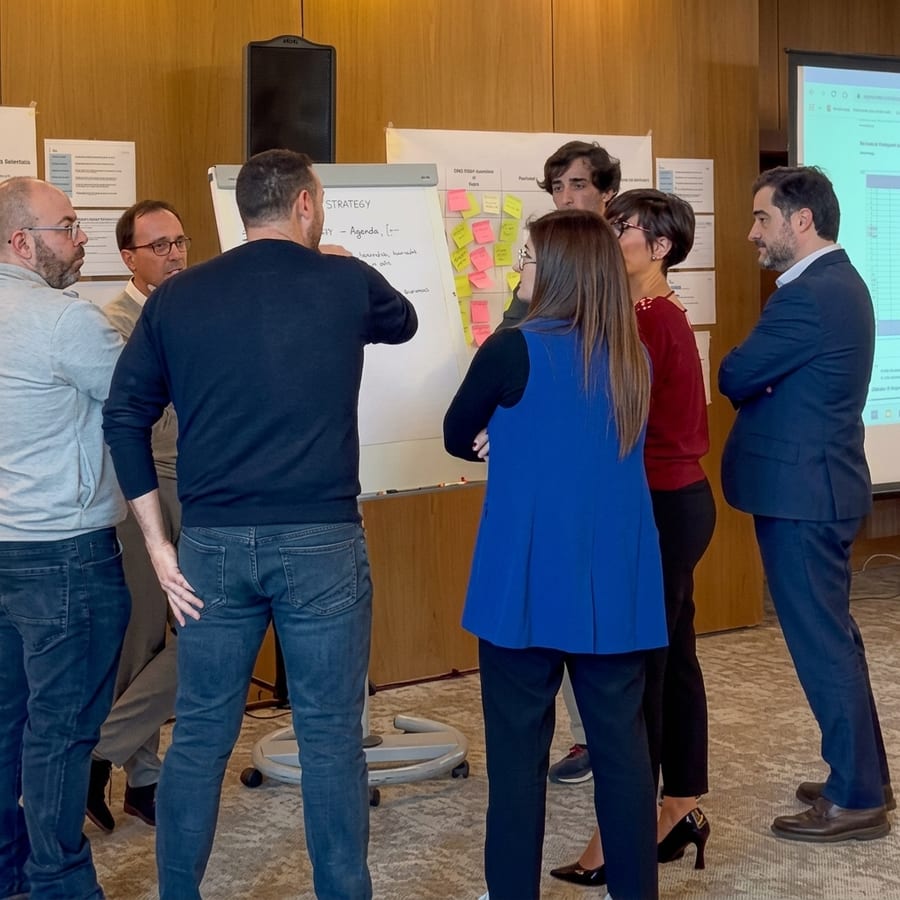 Colaboradores em pé à volta de um quadro coberto de post-its, numa sessão de trabalho sobre a estratégia.