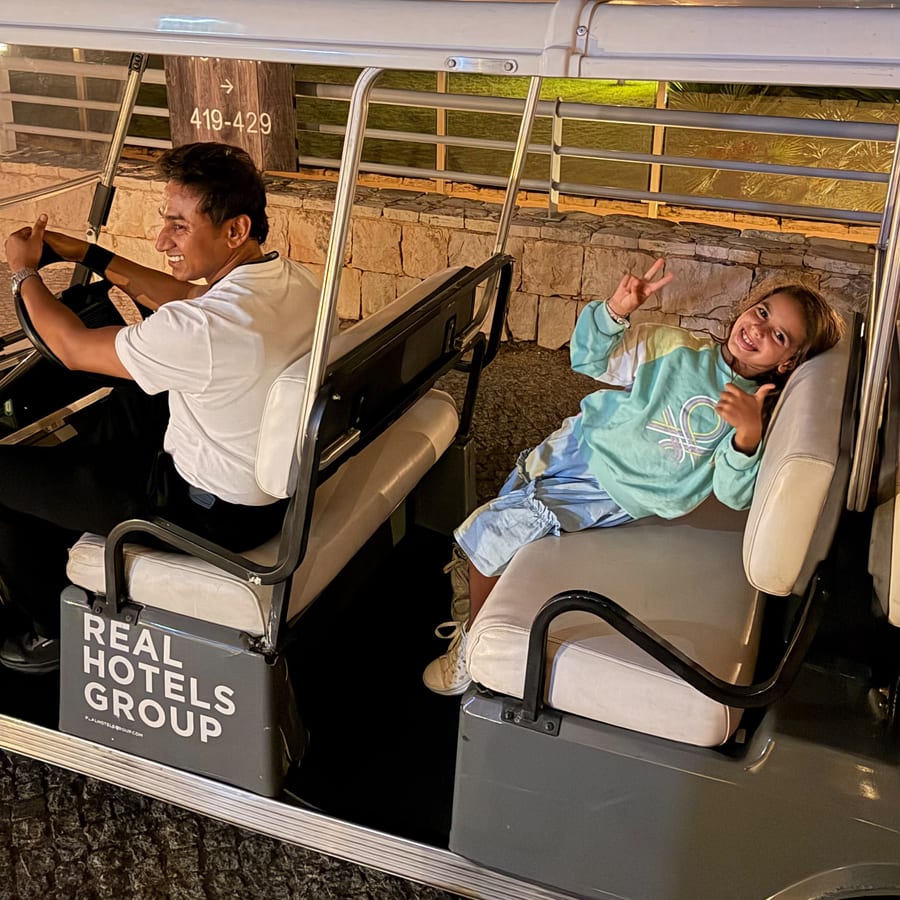 Um colaborador a conduzir um buggy de transfer do Real Hotels Group, com uma criança a acenar no banco de trás.