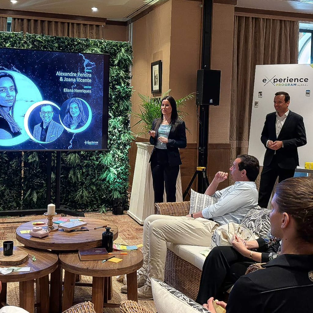 Uma sessão do eXperience Program num lounge de hotel: colaboradores sentados em sofás, de frente para um ecrã e dois oradores.
