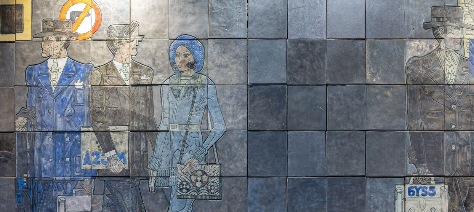 Um mural de azulejos com figuras em marcha, de pastas e sacos na mão, em azuis e cinzentos sobre azulejo vidrado.