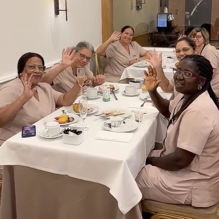 Uma equipa de andares sentada a uma mesa posta, a acenar e a sorrir durante a sua semana de reconhecimento.