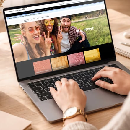 A plataforma Real People aberta num portátil, com a página inicial a mostrar colaboradores e as secções do site.
