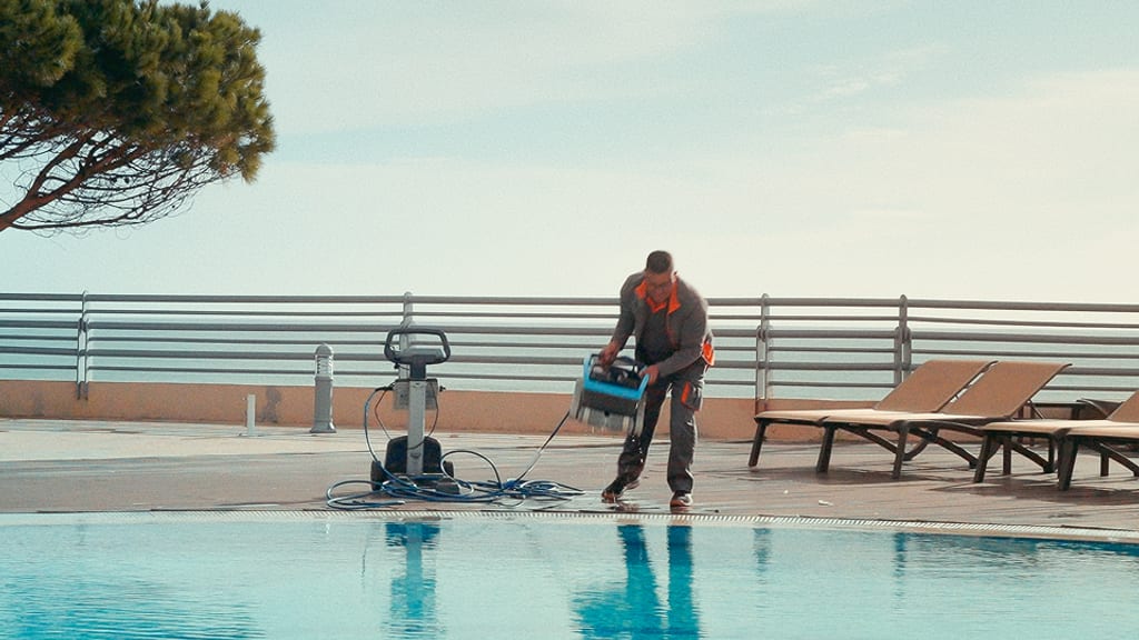Um técnico a fazer manutenção de equipamento no terraço da piscina de um hotel, ao início da manhã.