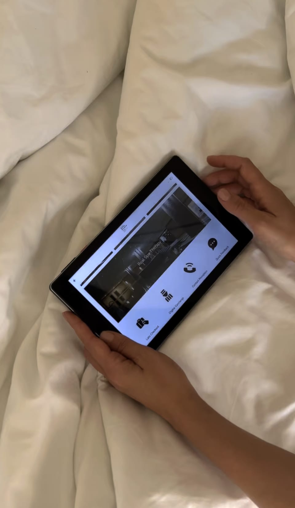 Um hóspede a usar o tablet SuitePad do quarto, na cama.