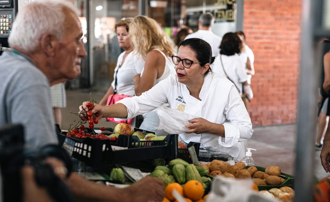 Uma chefe a escolher fruta e legumes numa banca de mercado local.