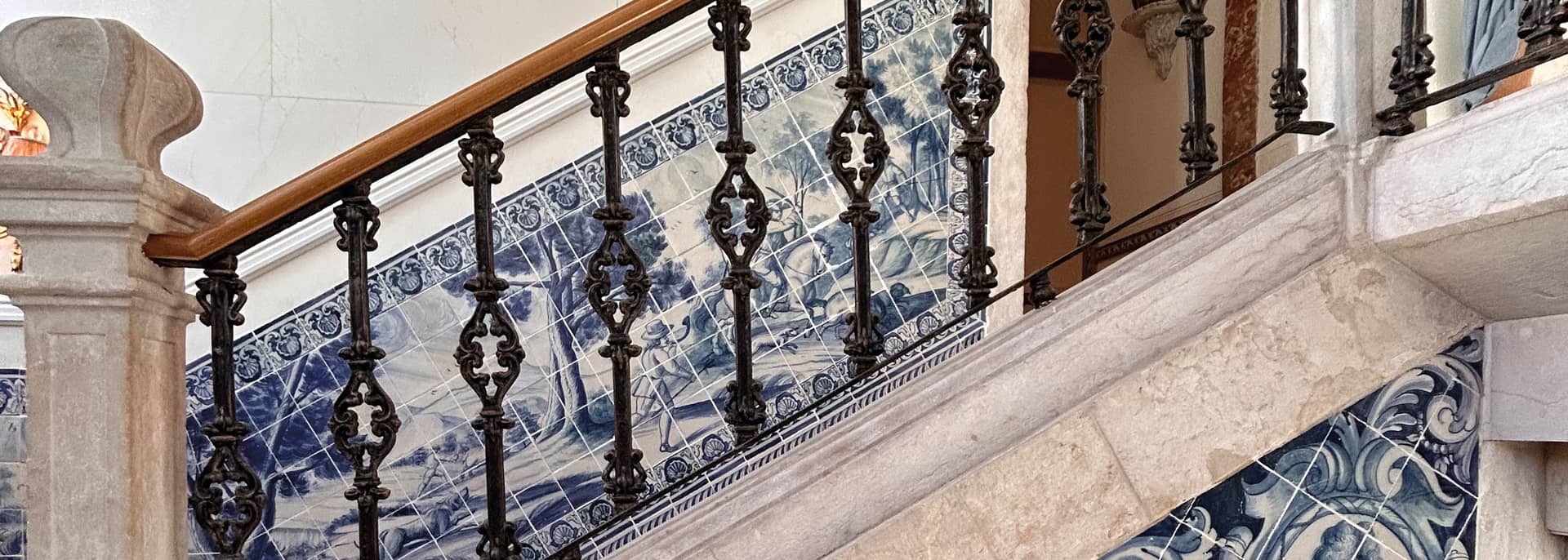 Escadaria de hotel com balaustrada de ferro e painéis de azulejo azul e branco.