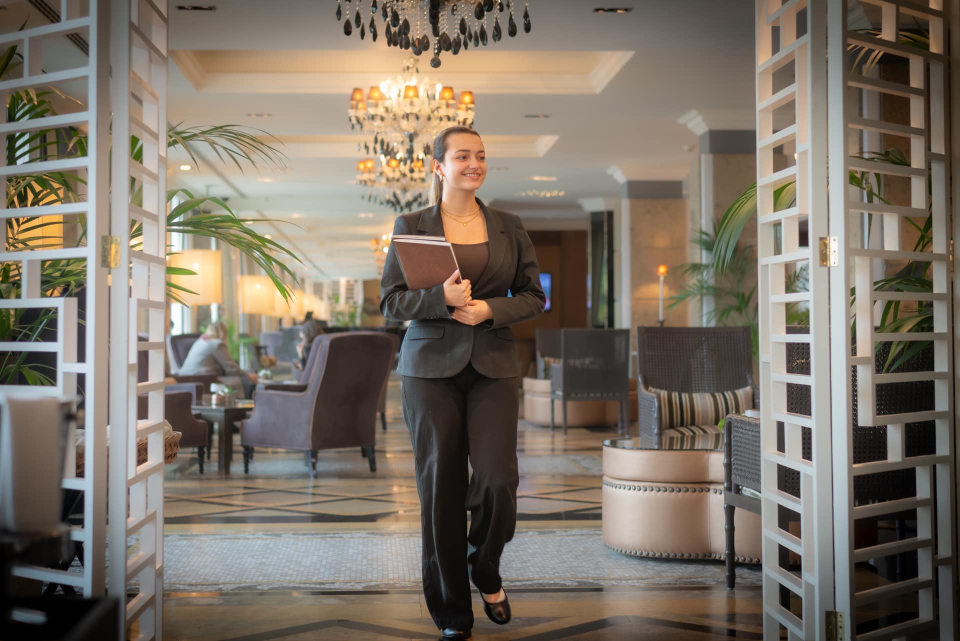Uma colaboradora atravessa o lounge de um hotel, com pastas debaixo do braço.